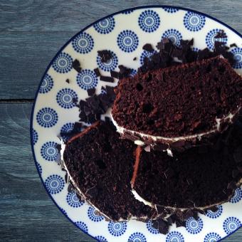 Auf einem blau grauen Untergrund steht ein ein weißer Teller mit blauem Muster. Darauf liegen drei Stücke Rote Bete-Schokokuchen, dieser sieht fluffig und saftig aus.