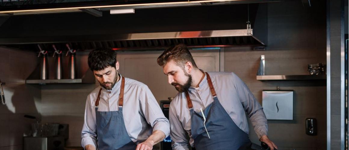 Zwei Köche stehen mit Schürze am Herd und bereiten eine Mahlzeit zu